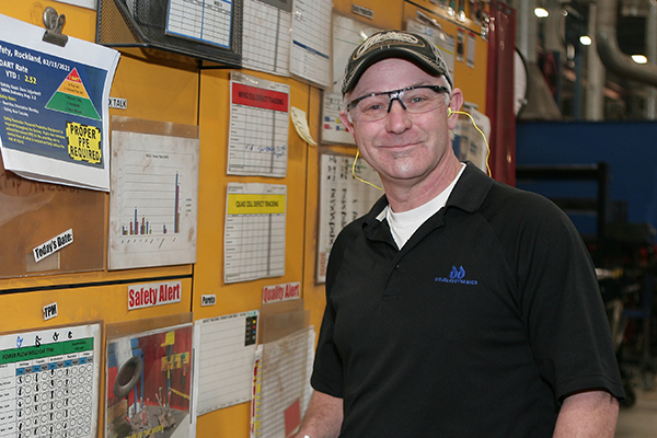 Man with safety glasses stands in front of a board with safety messages on it