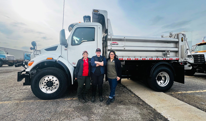 Three women in front of a large dump truck.